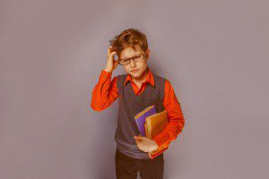 European-looking boy  of ten years  in glasses thinking intently book on a blue background retro