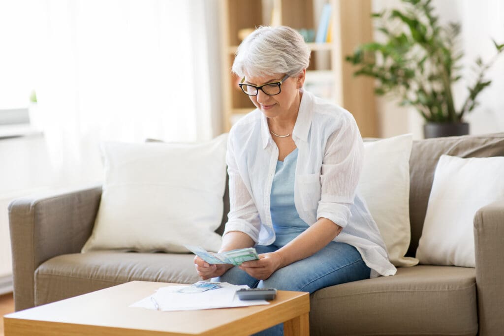 Older woman reviewing her finances and counting money on the couch at home