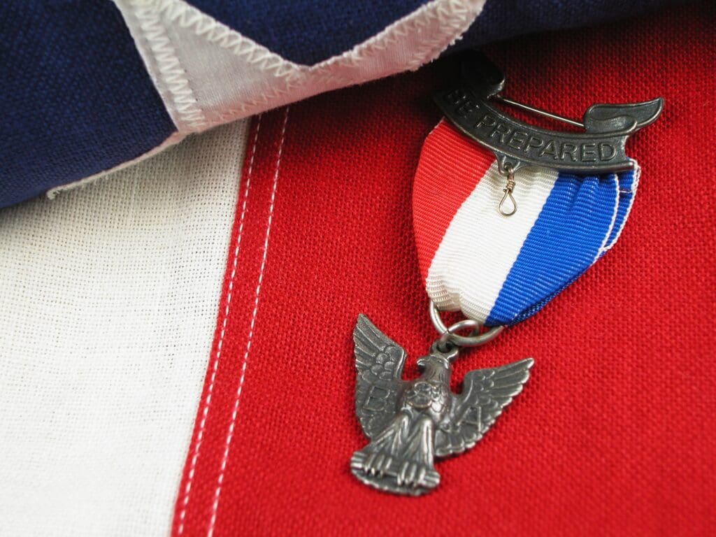 Eagle Scout medal with "Be Prepared" bar and eagle pendant resting on a red, white, and blue American flag