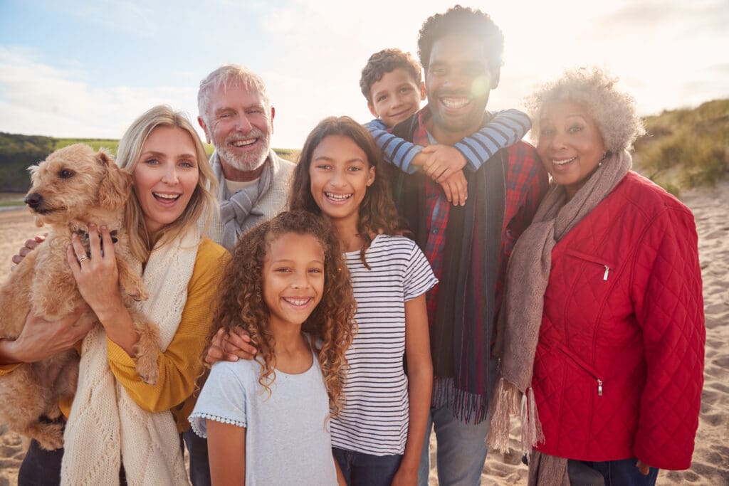 Smiling multigenerational family of three generations standing together with their dog on a sandy beach at sunset